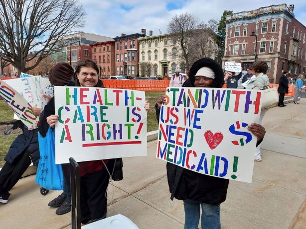 Two Self Advocates hold up signs saying: HEALTH-CARE IS A RIGHT! (Right is underlined) And STAND WITH US WE NEED MEDICAID!